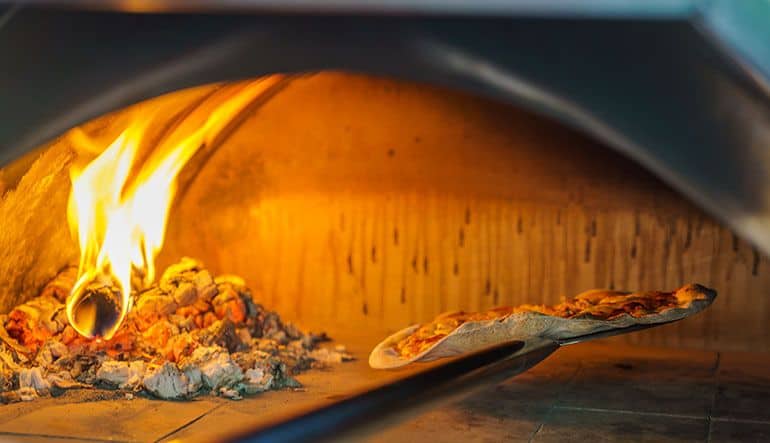 pizza being added to wood and coal burning oven