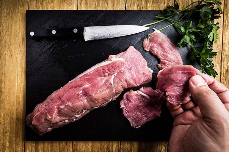 raw pork tenderloin on black cutting board with cutting knife and parsley seasoning