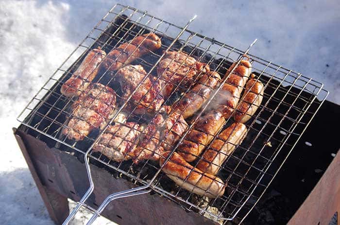 sausages and chicken cooking in grill cage over old barbecue