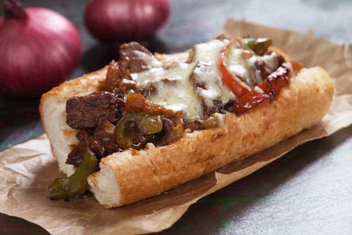 grilled strips of beef steak served with green and red peppers in baguette bread, and with cheddar melted on top