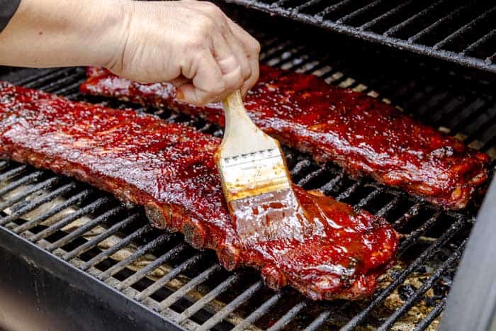 painting pork ribs with bbq sauce while on charcoal grill grates