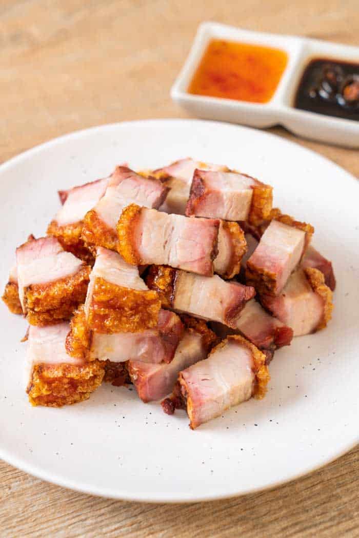 smoked pork belly cubes served on white plate with dipping sauces