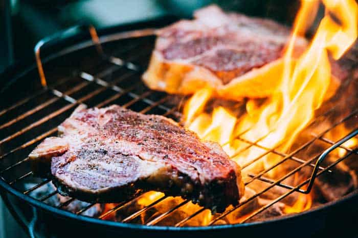 Two t-bone florentine beef steaks on the grill with flames