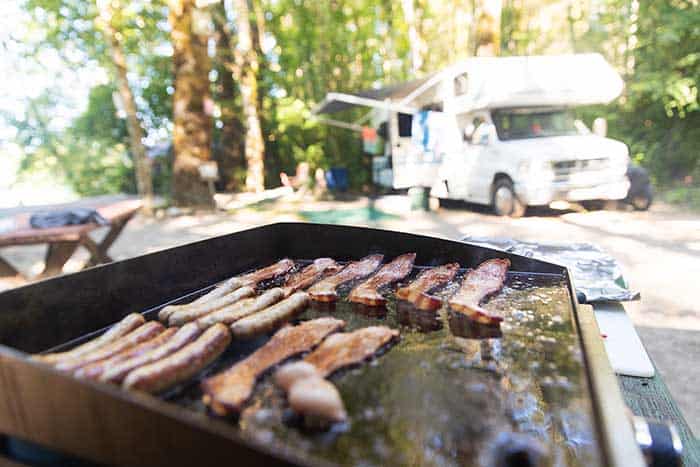 hot breakfast on a flat grill outside featuring bacon and sausage