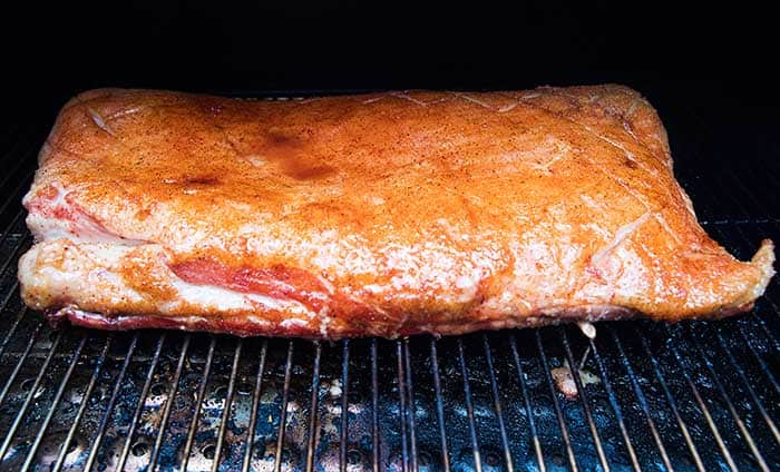 large pork belly on smoker grates