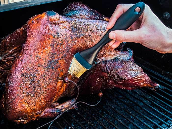 basting barbecue turkey on smoker in butter solution