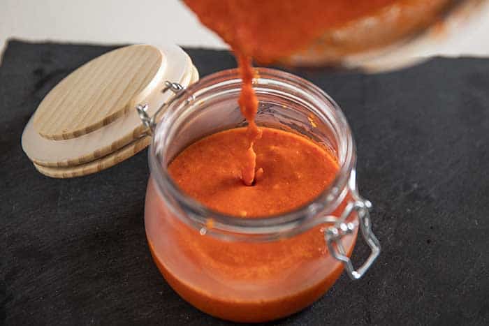 pouring smooth cayenne bbq sauce into mason jar for storage