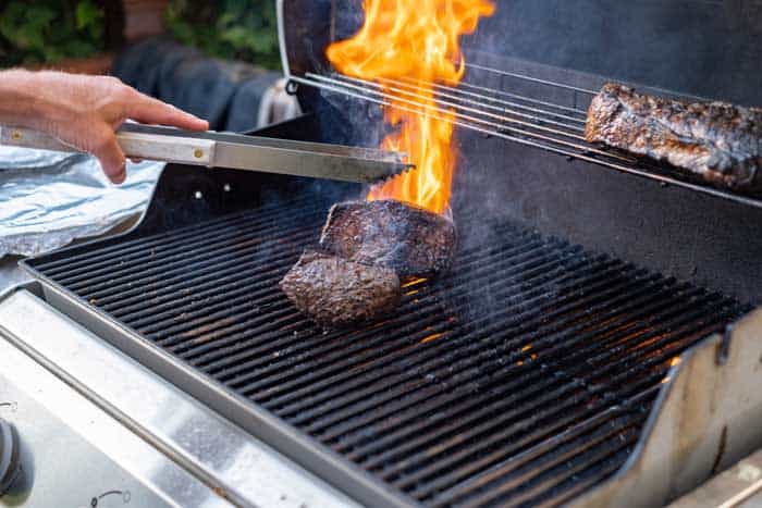 flare-up on gas grill man cooking beef on the grill outside flipping the meat with tongs