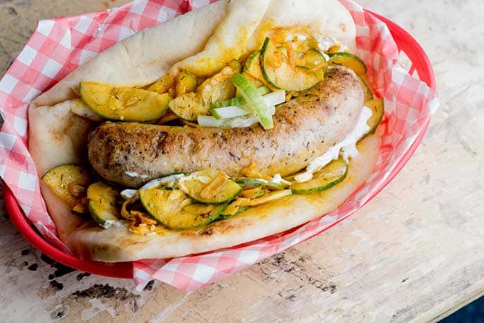 grilled bratwurst served in toasted flatbread and onion zucchini sauerkraut and yellow mustard dressing