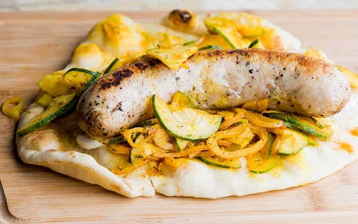 grilled bratwurst served in toasted flatbread and onion zucchini sauerkraut and yellow mustard dressing