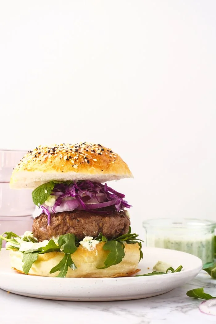 grilled lamb burger served in a hamburger bun and topped with fresh lettuce, feta cheese, and sliced red onion