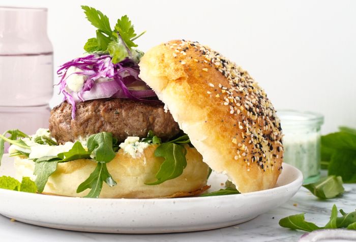 grilled lamb burger served in a hamburger bun and topped with fresh lettuce, feta cheese, and sliced red onion