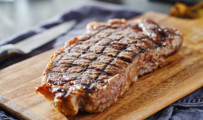 grilled new york strip steak resting on wooden cutting board