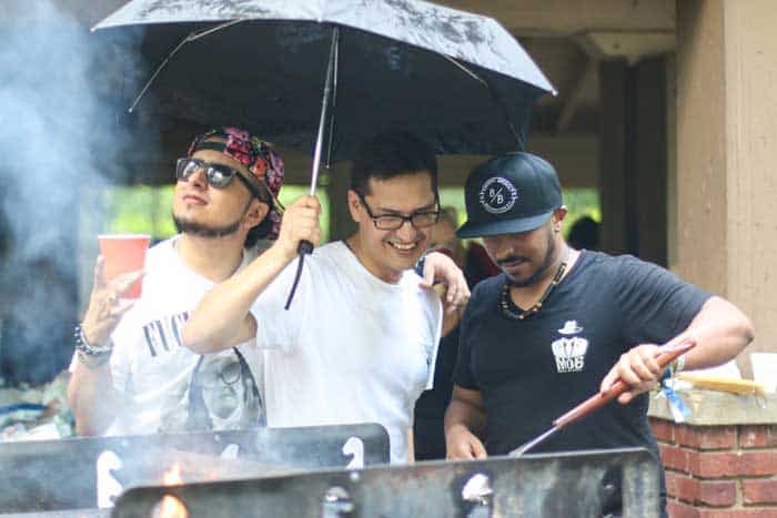 friends grilling outside in rainy wet weather using large umbrella for shelter