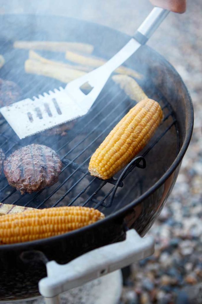 grill spatula being used on charcoal grill cooking corn and burgers