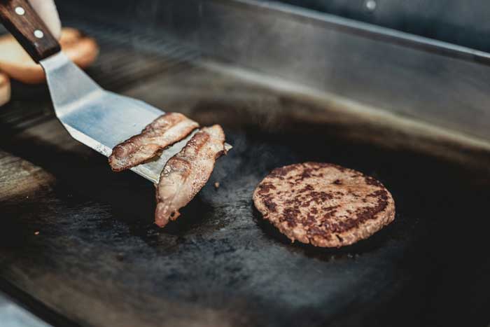 grill spatula on flat top grill with bacon and burgers