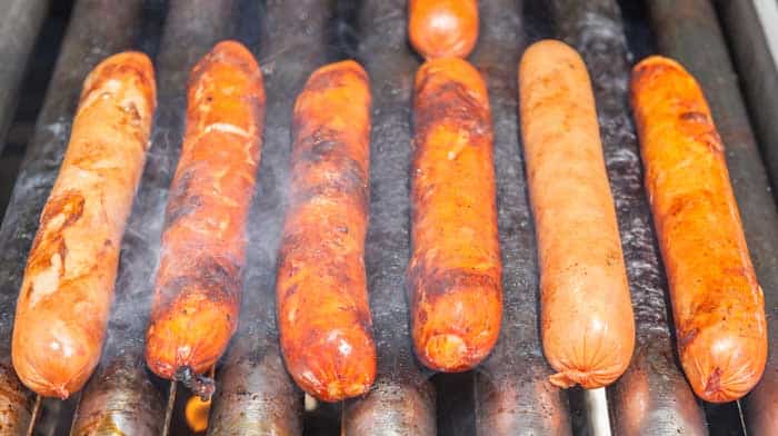 hot dogs coated in mustard and bbq rub on smoker grates