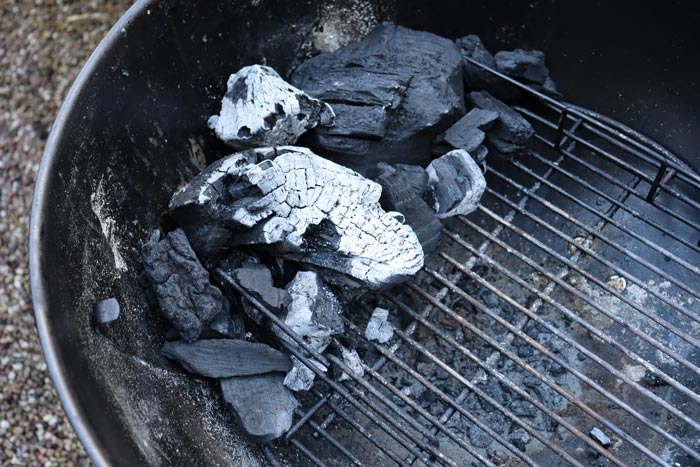 lump charcoal pieces arranged to one side on grill grates