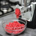 meat grinder grinding beef into clear kitchen bowl