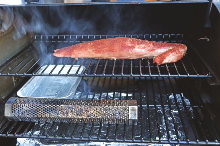 pork tenderloin being smoked on pellet grill with tube smoker lit underneath