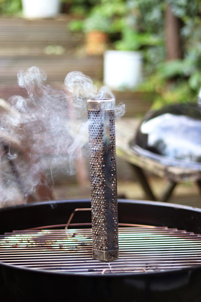 pellet smoke tube sat on grill grates with smoke billowing out