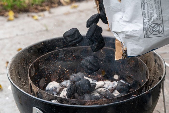 pouring fresh briquettes into a lit charcoal grill