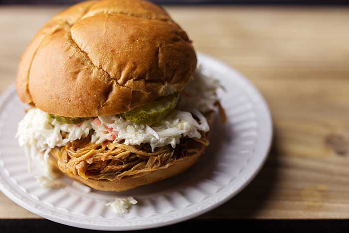 pulled pork BBQ sandwich with sweet pickles and coleslaw on a white plate