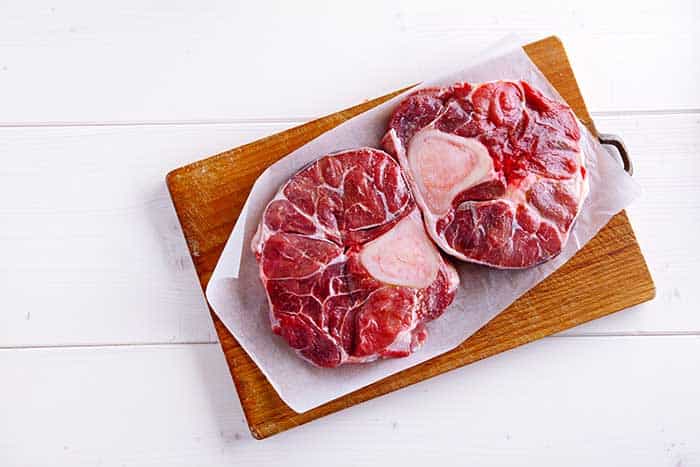 raw beef shank cross cuts presented on parchment paper and wooden chopping board
