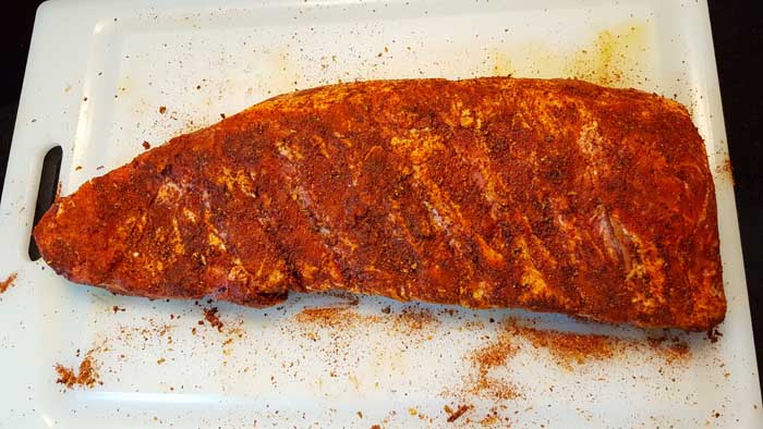 raw pork spare ribs with rib rub applied generously over both sides of rack