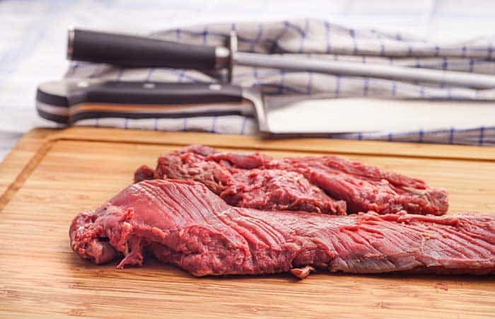 raw trimmed beef skirt steak on wooden chopping board