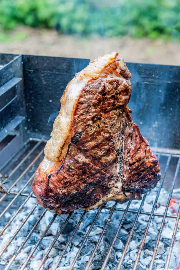 reverse seared t-bone steak sitting on charcoal grill grates