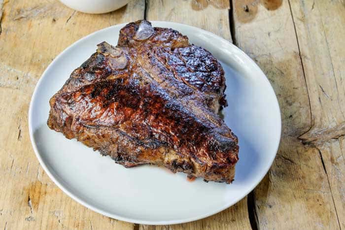 Round dish with grilled t-bone beef steak on wooden table