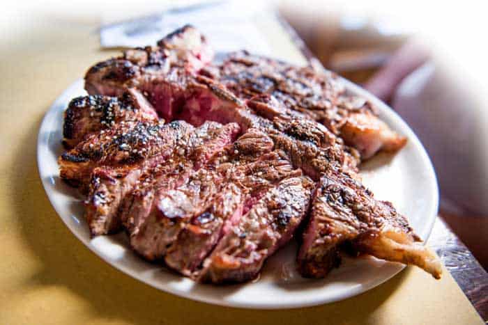 White round plate with cut grilled T-bone steak isolated on the table