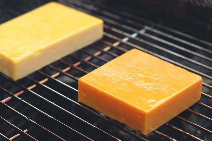 red leicester and cheddar cheese during cold smoking process on charcoal grill grates