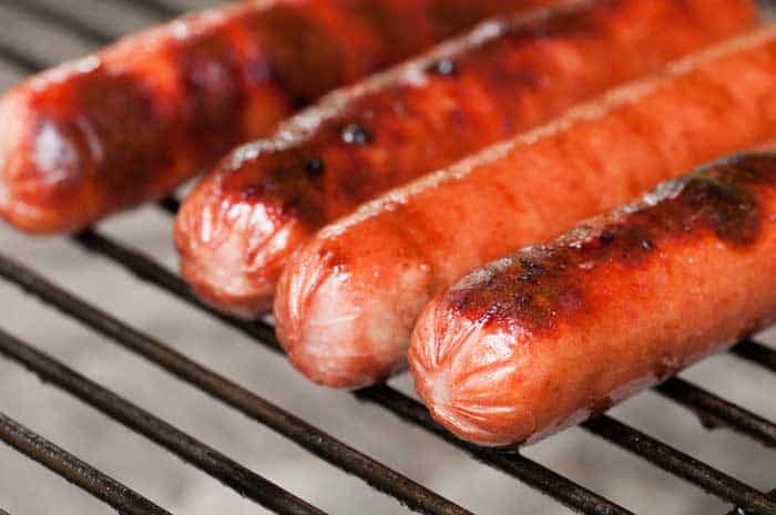 Four hot dogs getting nicely done on a charcoal grill