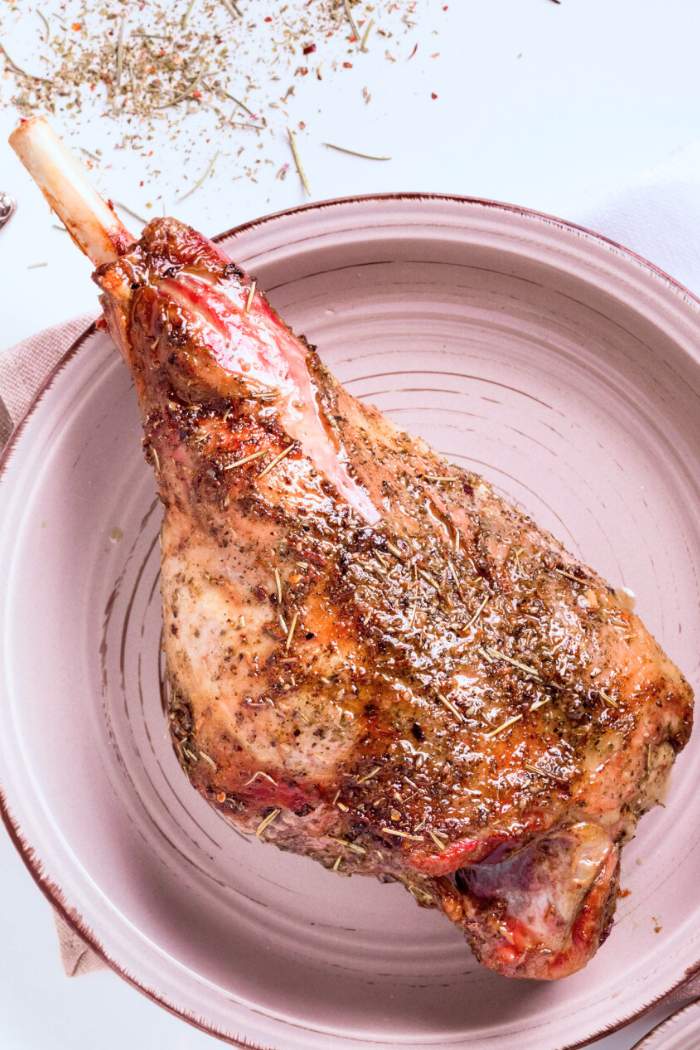 whole bone-in smoked leg of lamb pulled from bbq smoker with spice and pepper dry rub