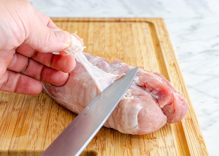 trimming fat and silverskin from pork tenderloin on wooden chopping board