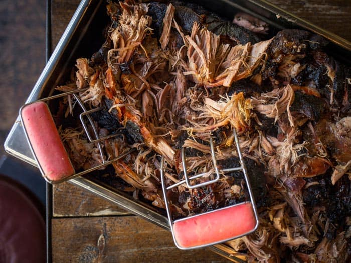 shredded pulled pork butt in aluminum pan with meat shredders