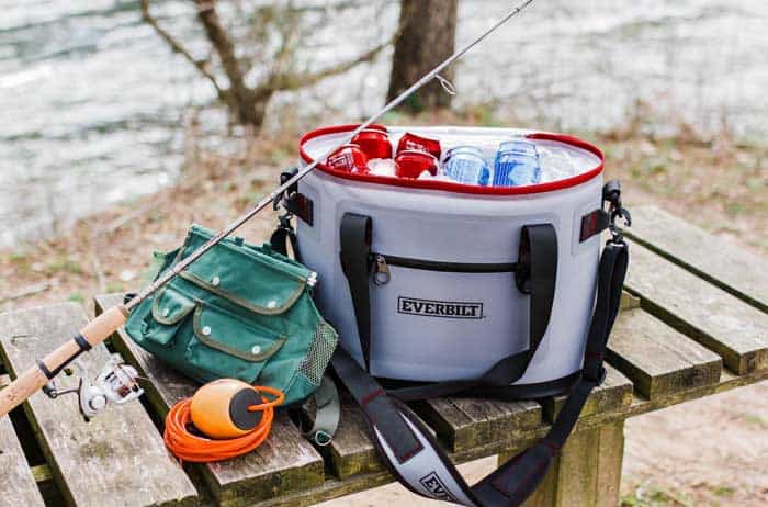 soft sided cooler containing drinks and ice resting on bench with fishing outdoor gear