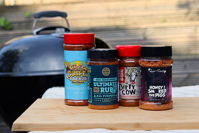 store-bought bbq dry rubs outside on wooden block with view of charcoal grill behind