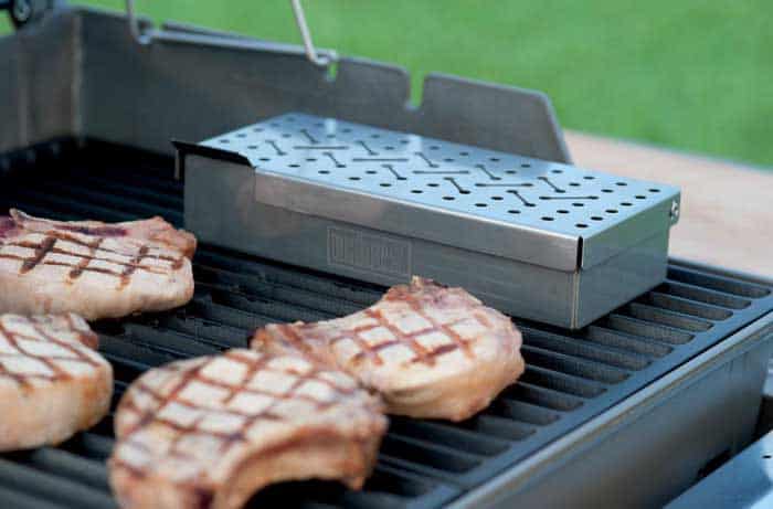 rectangle smoker box on grill grates next to pork meat